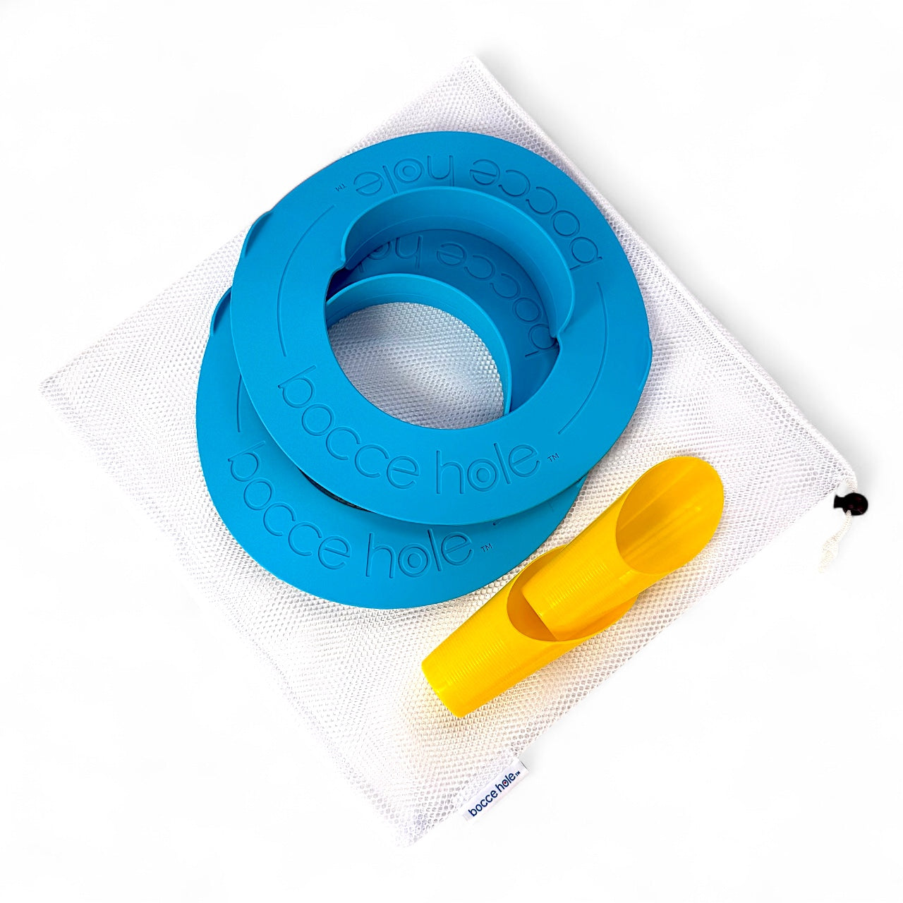 Bocce Hole Rings and Scoops (Only) set pieces displayed on a white surface.  Two 100% silicone scoring rings, two yellow sand scoops, both of which are laying atop a white branded mesh carry bag.   